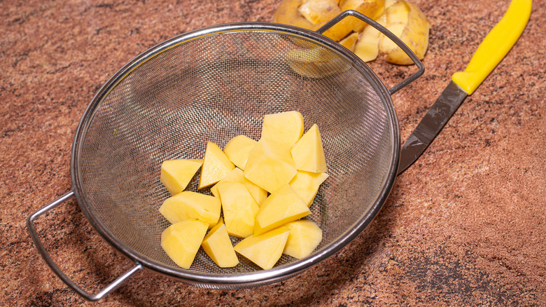 Diced potatoes sit in a metal mesh collander