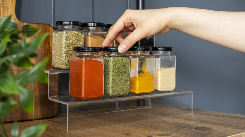 A hand reaches for unlabeled spices on a clear plastic rack