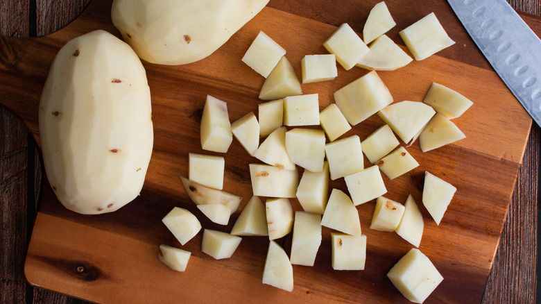 Whole and diced potatoes on a cutting board with a knife