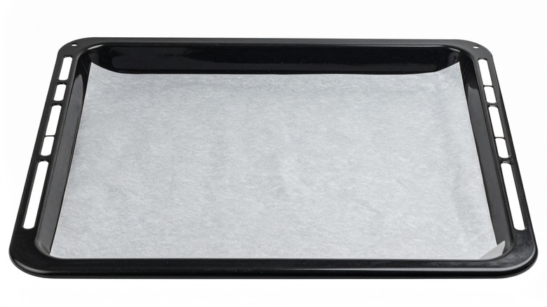 A black metal baking sheet is prepped with a piece of parchment paper
