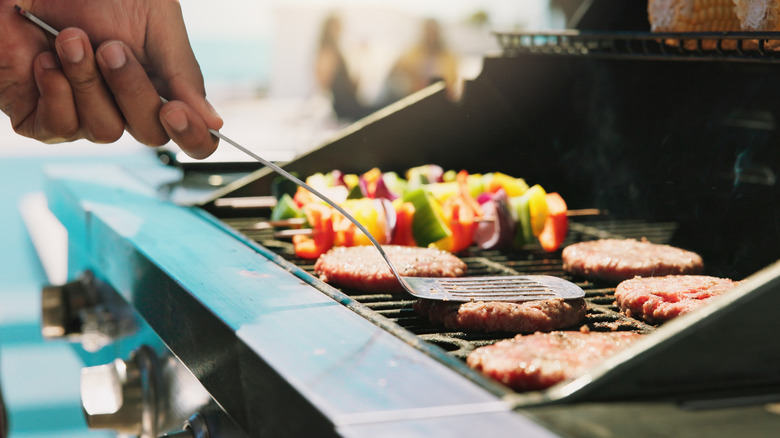 A hand pushes down a burger on a grill