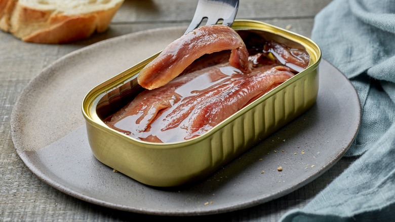 Anchovies in a can with a fork lifting one piece