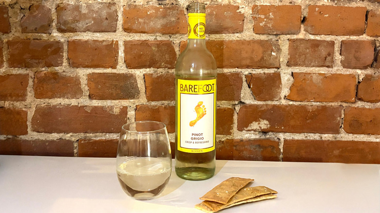 A bottle of Barefoot Pinot Grigio with a poured glass next to it and three crackers against a brick background