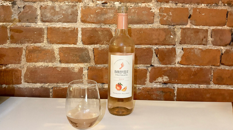 A bottle of Barefoot Peach Fruitscato with a poured glass next to it against a brick background
