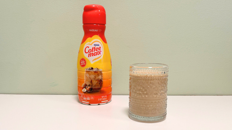A cup of coffee next to a container of Coffee Mate Hazelnut Coffee Creamer
