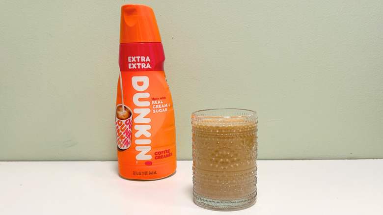 A cup of coffee next to a bottle of Dunkin' Extra Extra Coffee Creamer