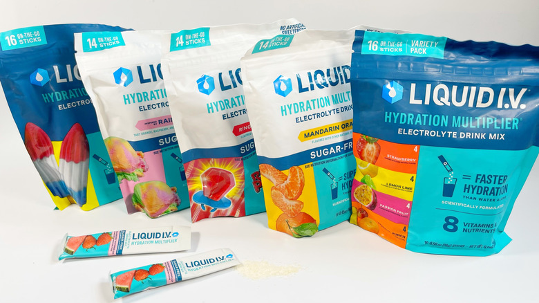 Several bags of different kinds of Liquid I.V. With one stick spilling powder on a white background