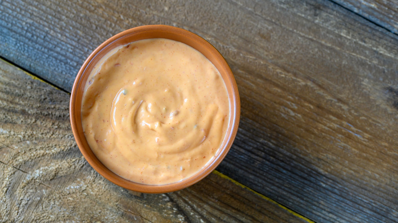 A bowl of creamy pink sauce sits on a wooden table