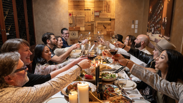 A group of friends toast at a banquet-style dinner table