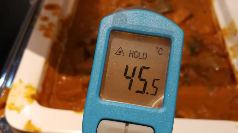 An infrared thermometer is held above a buffet dish, with the thermometer displaying 45.5 degrees Celsius