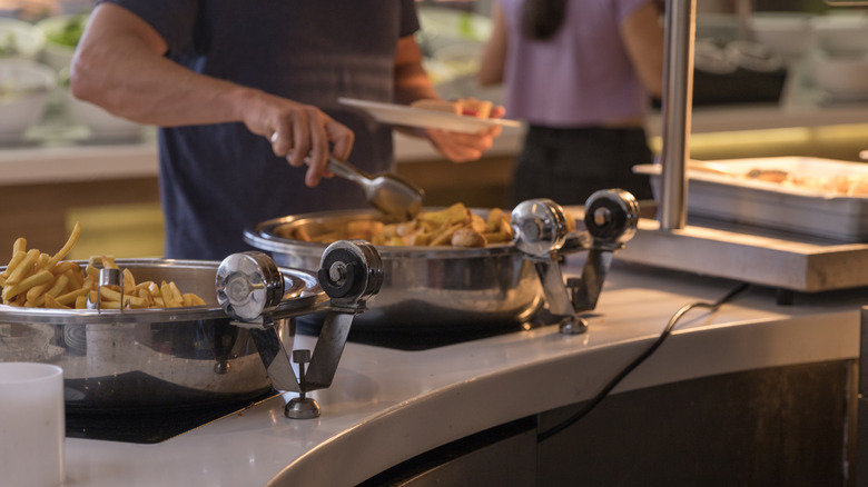 A man uses tongs to put food onto his plate at a buffet