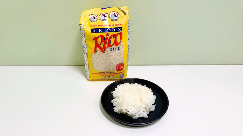 A bag of Arroz Rico Medium Grain Rice next to a black plate of rice