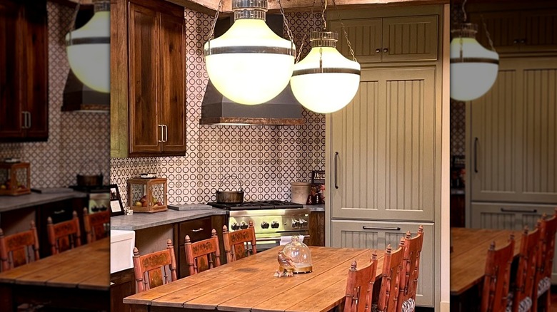 A small kitchen with large light fixtures, wooden cabinets, and patterned wallpaper