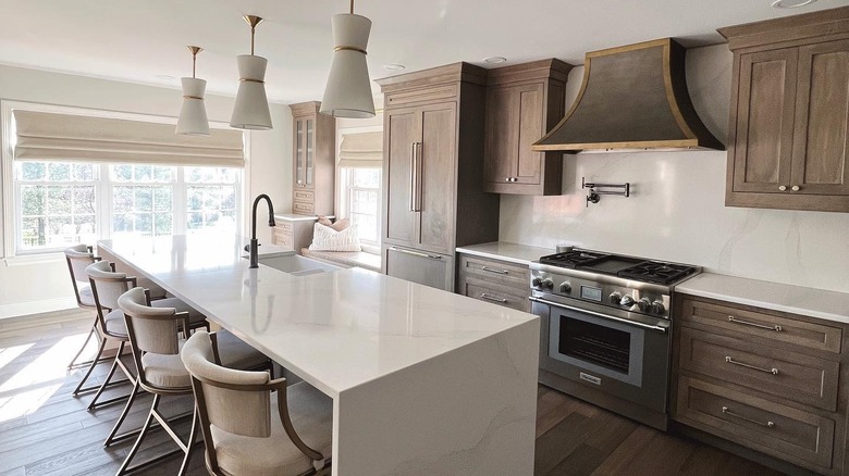 A modern white island in a large kitchen with a dark wood floor
