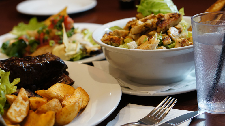 Plates of restaurant food, including a chicken salad and potato wedges, are displayed on a restaurant table