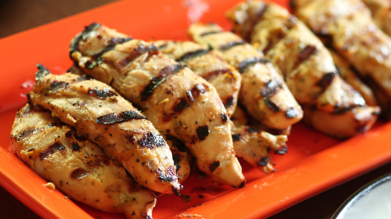 A pile of grilled chicken tenders on an orange plate