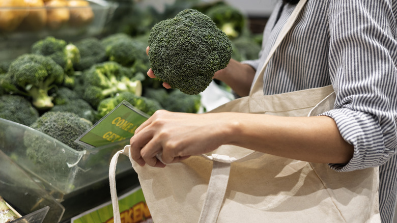 Woman putting broccoli into reusable shopping bag