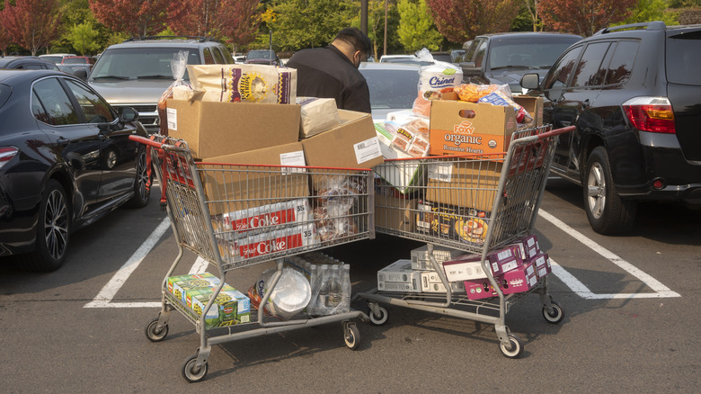 A person loads their car with two very full shopping carts of groceries