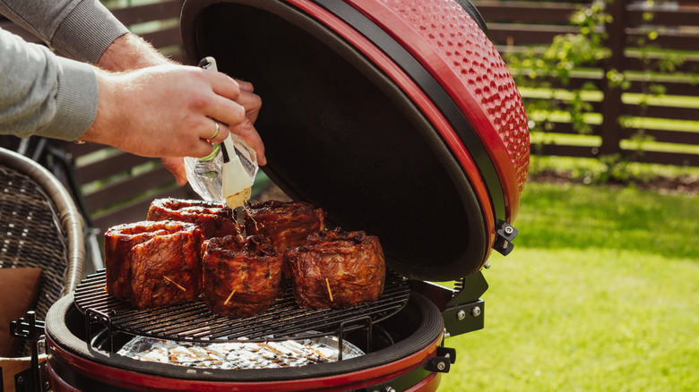 Hands brushing sauce on meat on a grill
