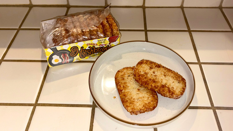 A package of hash browns next to a plate with two hash browns against a white tile countertop