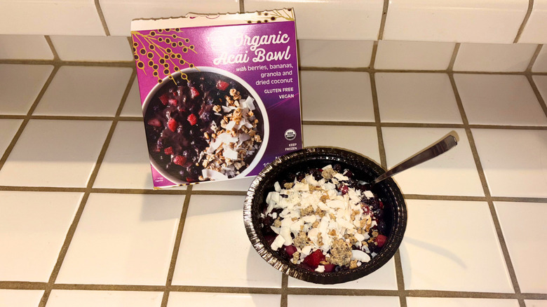 A package of an Organic Acai Bowl next to an acai bowl against a white tile countertop