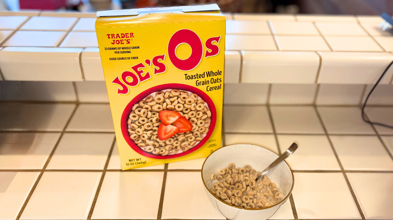 A box of Joe's Os next to a bowl and a spoon against a white tile countertop