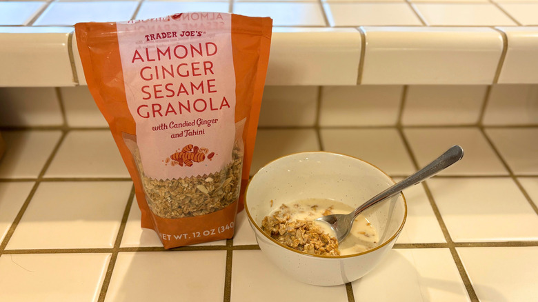 A package of Almond Ginger Sesame Granola next to a bowl and a spoon against a white tile countertop