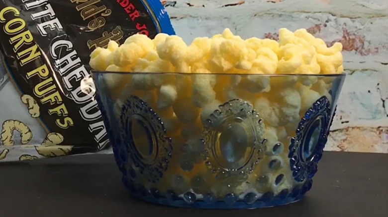 A bowl of Trader Joe's White Cheddar Corn Puffs next to a package of the item