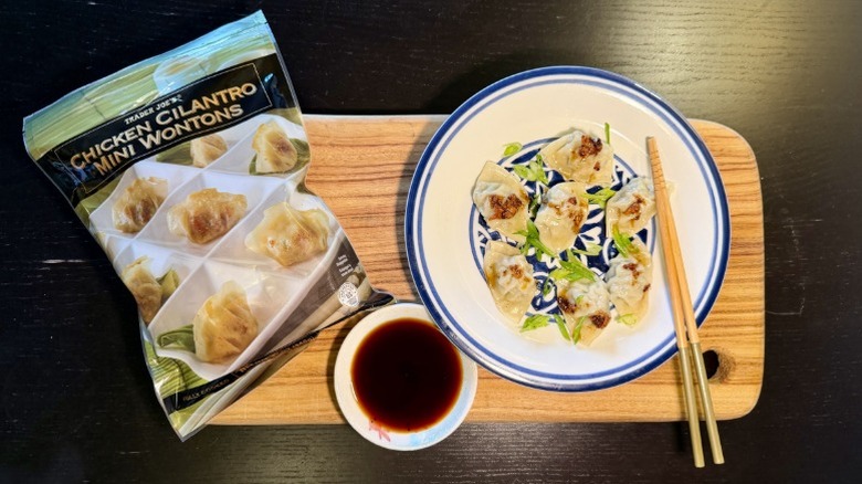Trader Joe's Chicken Cilantro Mini Wontons on a plate next to their packaging, a bowl of soy sauce, and chopsticks