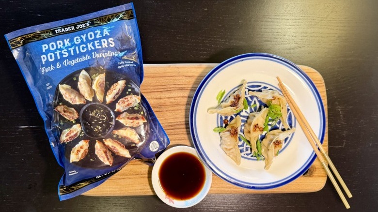 Trader Joe's Pork Gyoza Potstickers on a plate next to their packaging, a bowl of soy sauce, and chopsticks