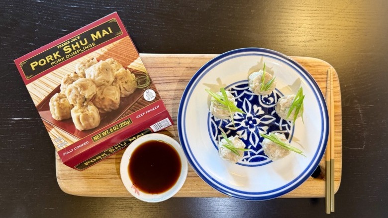 Trader Joe's Pork Shumai on a plate next to their packaging, a bowl of soy sauce, and chopsticks