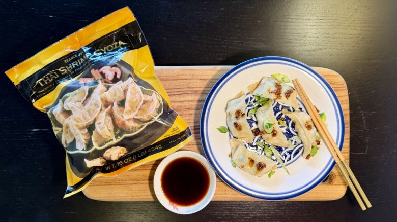 Trader Joe's Thai Shrimp Gyoza on a plate next to their packaging, a bowl of soy sauce, and chopsticks