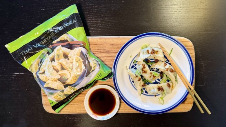 Trader Joe's Thai Vegetable Gyoza on a plate next to their packaging, a bowl of soy sauce, and chopsticks