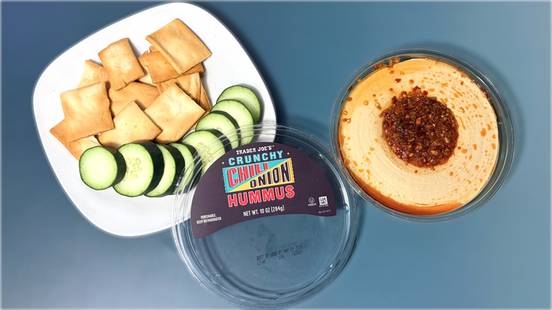 Open container of Trader Joe's hummus with plate of crackers and vegetables