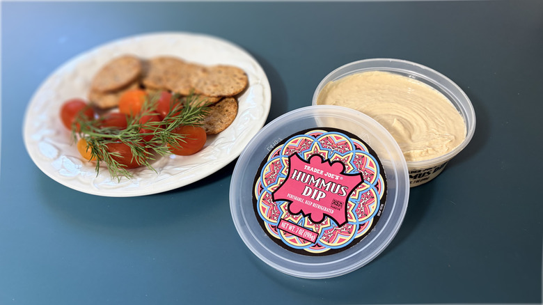 Open container of Trader Joe's hummus with plate of crackers and vegetables