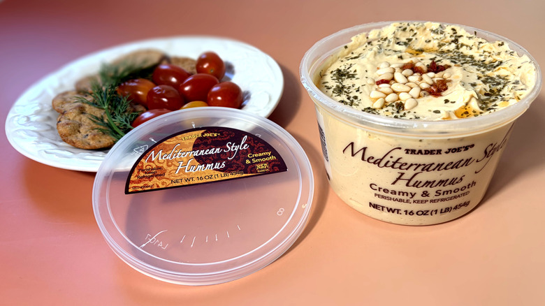 Open container of Trader Joe's hummus with plate of crackers and vegetables