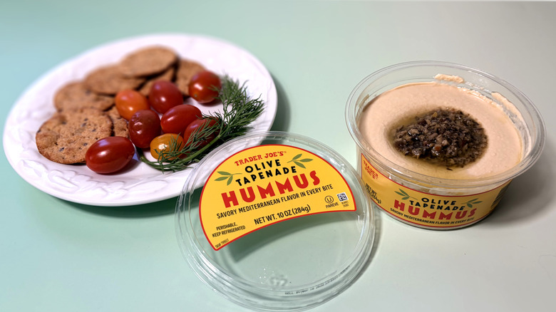 Open container of Trader Joe's hummus with plate of crackers and vegetables