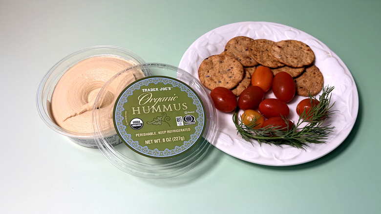 Open container of Trader Joe's hummus with plate of crackers and vegetables