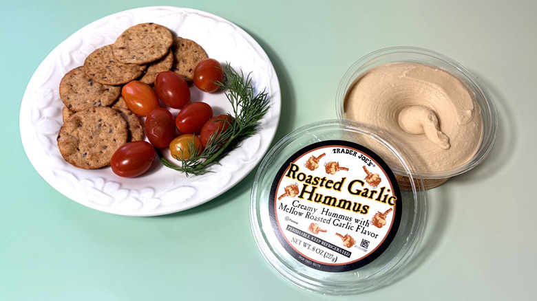 Open container of Trader Joe's hummus with plate of crackers and vegetables