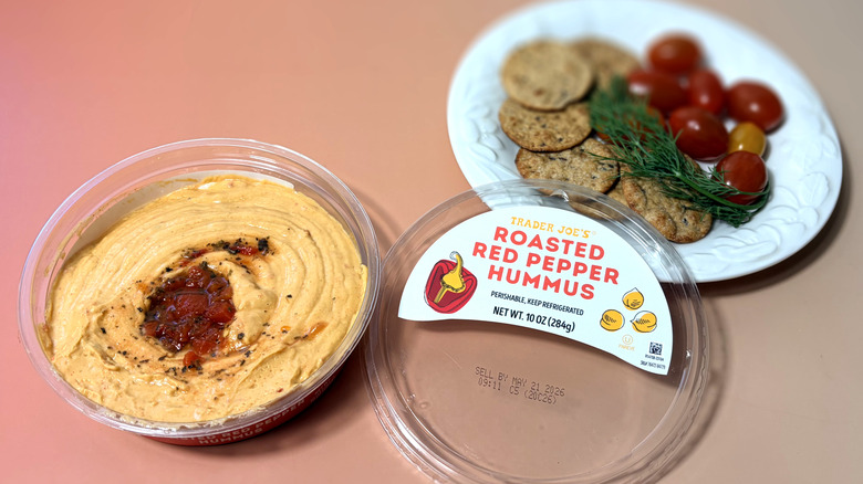 Open container of Trader Joe's hummus with plate of crackers and vegetables