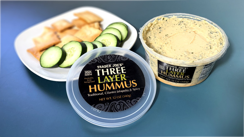 Open container of Trader Joe's hummus with plate of crackers and vegetables