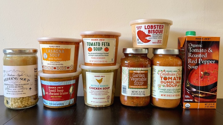 A lineup of Trader Joe's soups, including Italian-style Wedding Soup, Lasagna Soup, Lentil Soup with Ancient Grains, Tomato Feta Soup, Kettle Cooked Chicken Soup, Lobster Bisque, Garden Vegetable, Calabrian Chili Tomato Dumpling, and Organic Tomato and Roasted Red Pepper