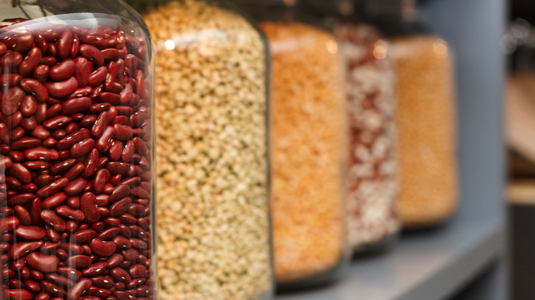 A close-up of glass jars of beans and grains lined up in a pantry