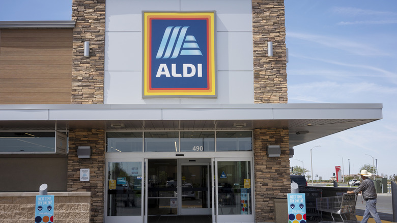 A man in a white cowboy hat walks into Aldi with a cart