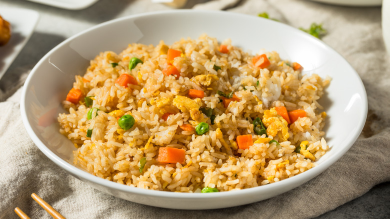 A white bowl of fried rice featuring peas and carrots