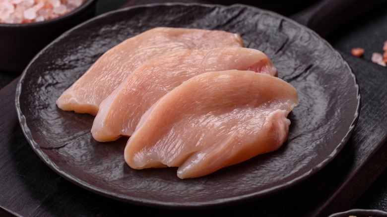 A black plate with several slices of chicken breast on it