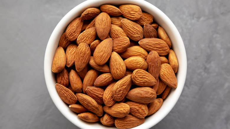 A white bowl full of almonds against a grey background
