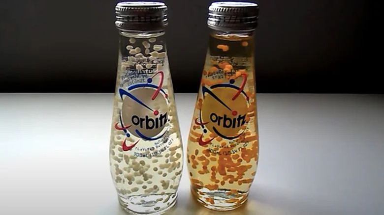 Two Orbitz soda bottles on a table, one clear and one orange.