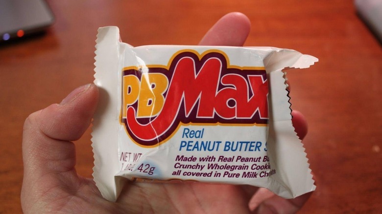 A hand holding a bag of PB Max candy bar