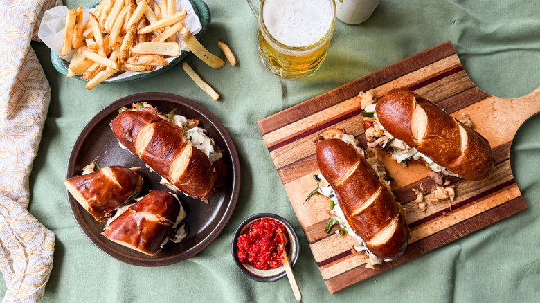 Chicken cheesesteak sandwiches on cutting board next to sandwiches on plate